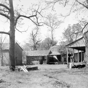 Brick house with covered porch and outbuildings among trees