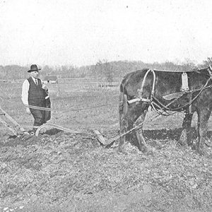 white man in overalls and white man in suit with a horse pulling a plow