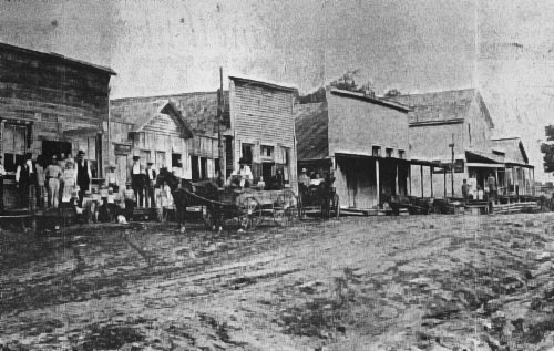 street scene with various storefronts and horse-drawn carts