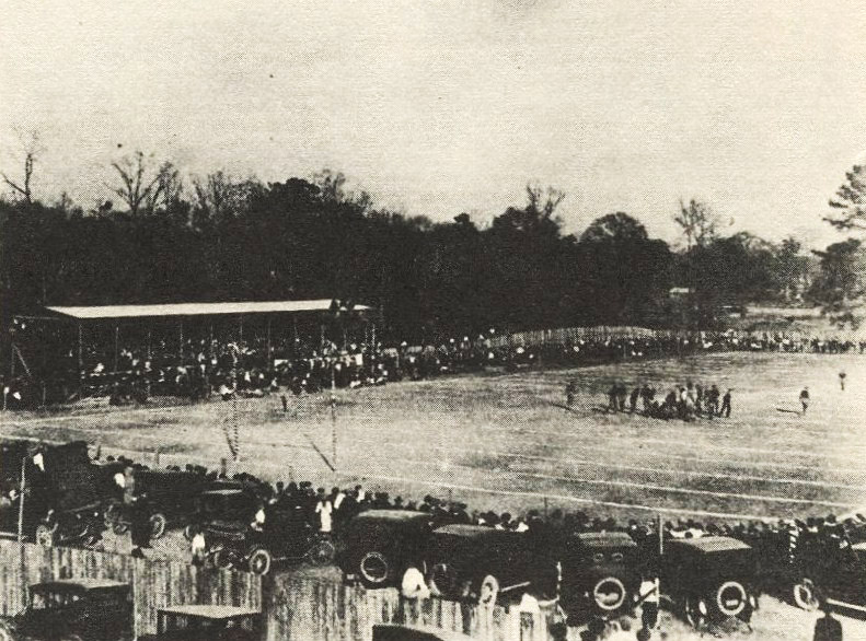Crowd of people and cars around football field during a game