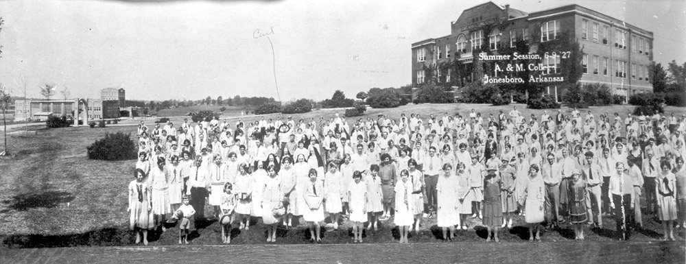 Group of white men and women lined up in field with three-story building behind them