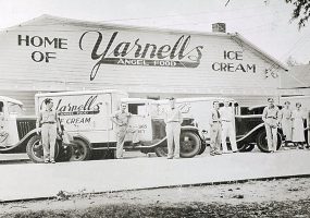 White drivers in uniform pose with their delivery trucks outside Yarnell's Angel-Food building