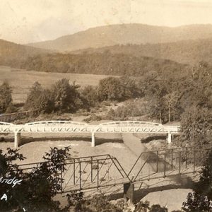 Aerial view of steel truss bridge and arched truss bridge over river with trees and mountains in the background