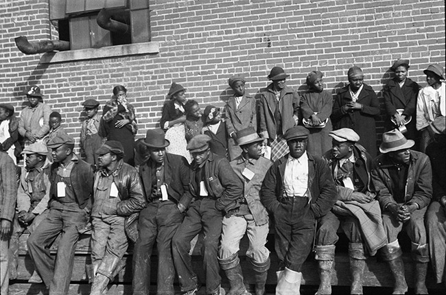 Group of African-American men and women with identification tags waiting outside brick building