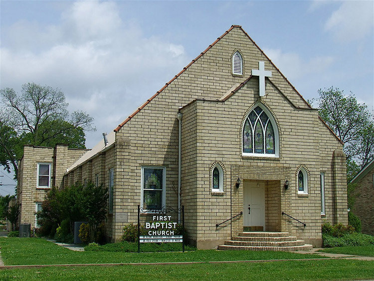brick church building with A-frame roof and arched windows with cross hanging above them and sign