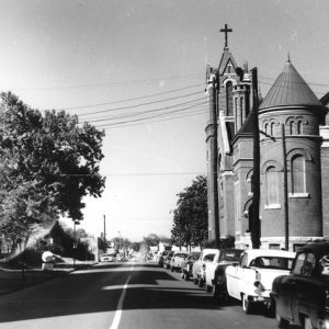 Street with ornate church and parked cars on the right and two-story building on the left