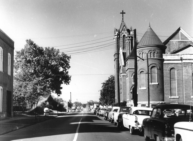 Street with ornate church and parked cars on the right and two-story building on the left