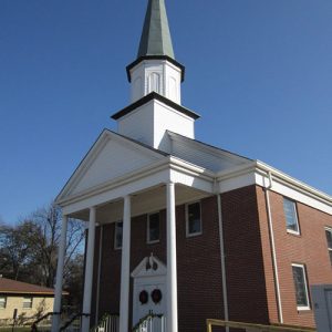Multistory brick church building with covered porch with four front columns and tall steeple on top