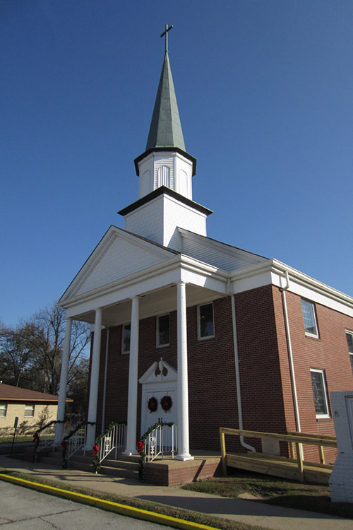 Multistory brick church building with covered porch with four front columns and tall steeple on top