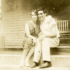 White man and woman sitting on porch with chair behind them