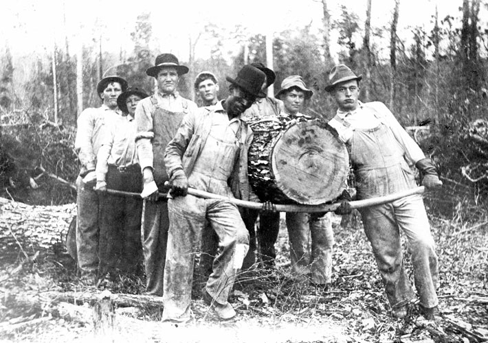 Mixed group of loggers carrying a large log using poles to support its weight
