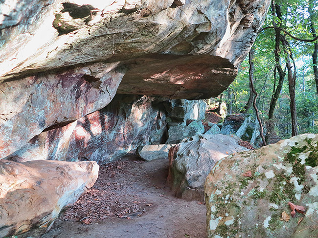 Walking path under rock outcropping with rock wall and trees