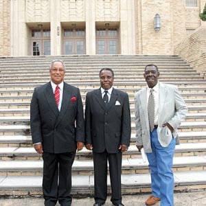 three African American men stand in front of stone steps leading to multistory stone building