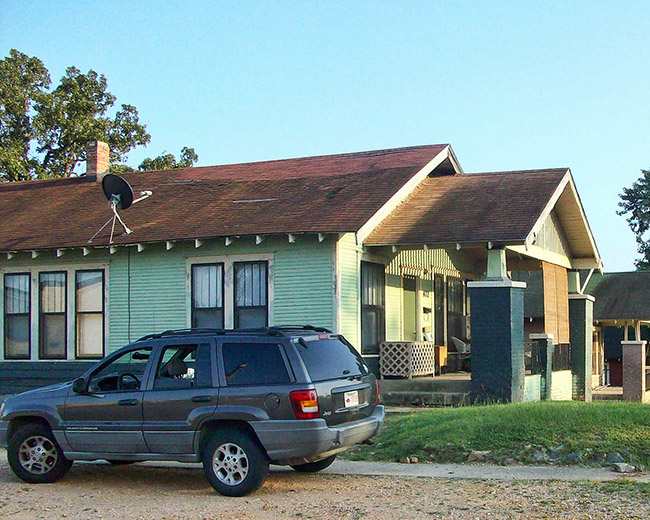 Side view of single-story house with covered porch and satellite dish on the roof with car parked beside it
