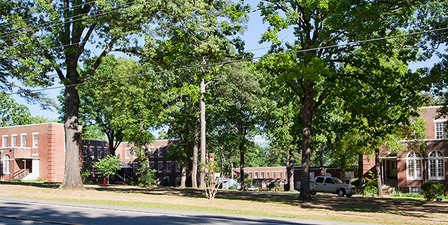 Two and three-story brick buildings with rows of windows surrounded by trees and street