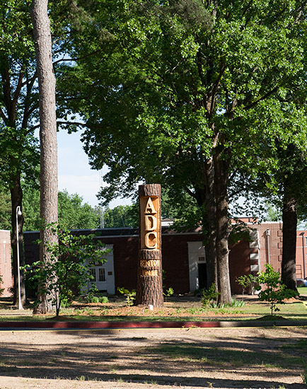 Log sign with "A.D.C. Benton Unit" carved into it with brick building and trees