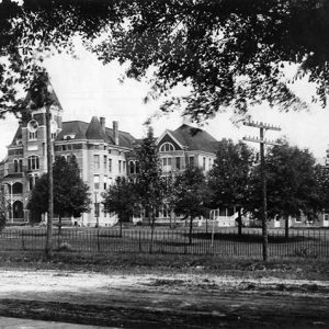 Three-story building with central tower and grounds with fence and power lines