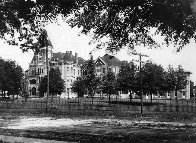 Three-story building with central tower and grounds with fence and power lines