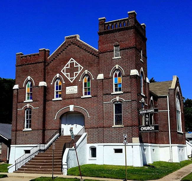 Multistory brick church building with arched multicolored windows and arched doorway on street corner