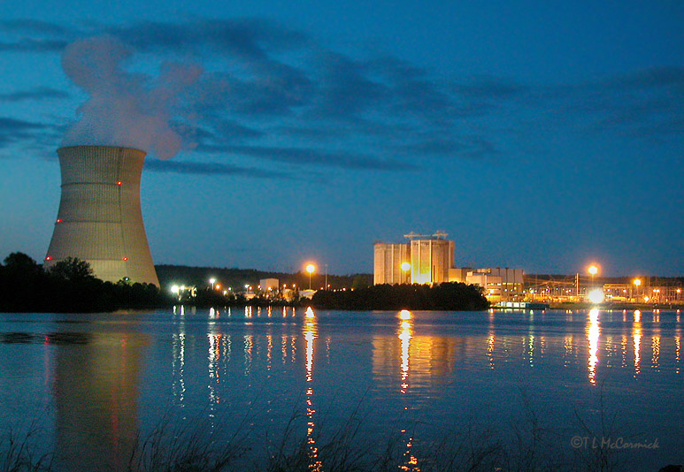 Cooling tower at night emitting steam by waterside power plant