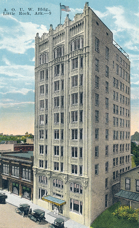 Ten-story building in between much smaller storefronts on city street with parked cars