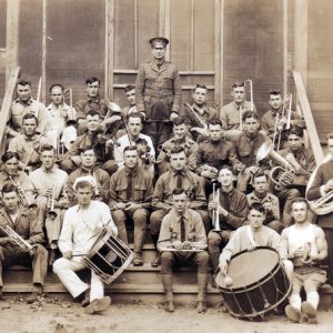 sepia toned photograph of group of men sitting on front steps of barracks holding various musical instruments