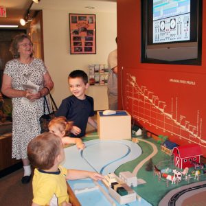 White woman views television display and white children play with model Arkansas River museum exhibition