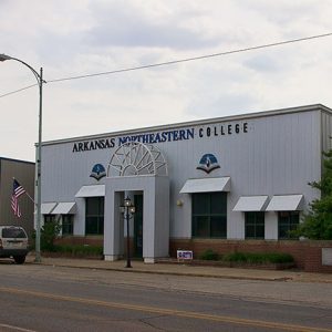 White building with blue lettering above the door and entrance gateway with arch on top and window awnings