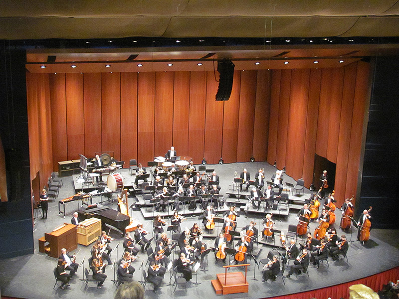 Orchestra members with instruments sitting on stage as seen from above