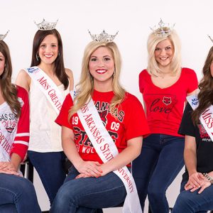 Five young white women with tiaras and sashes wearing A.S.U. tee shirts and blue jeans.