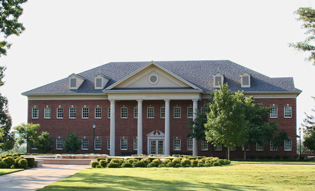 Two-story brick building with four columns and grounds
