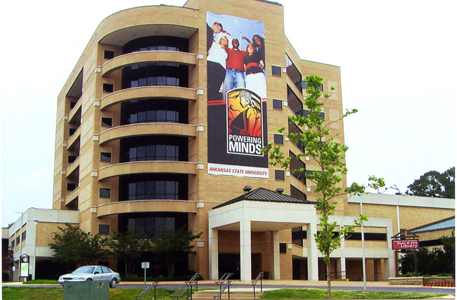 multistory brick and glass building with curved corner sporting large poster featuring diverse students