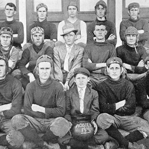 Group of young white men wearing football helmets with football labeled "Aggies 1911"