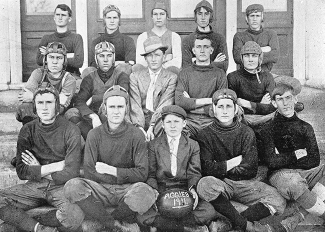 Group of young white men wearing football helmets with football labeled "Aggies 1911"