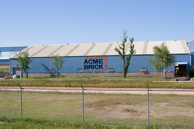 Large blue metal building with "Acme Brick" logo and fence