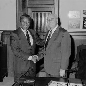 Older African-American man shaking hands with old white man with glasses in suit in office