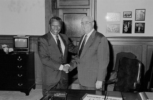 Older African-American man shaking hands with old white man with glasses in suit in office