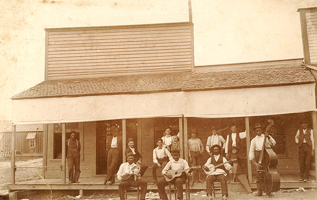 African-American musicians with their instruments and mixed group of patrons outside storefront building