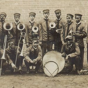 African-American brass band in uniforms with horns and drums posing outside brick building