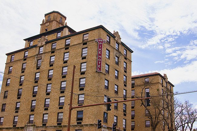 Multistory hotel building with cupola and red sign with white lettering hanging on corner facing street