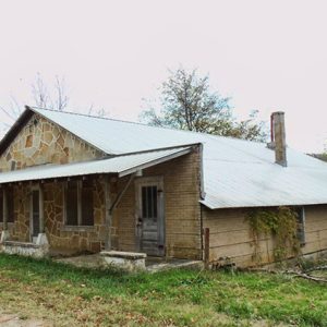Single-story storefront with stone front and covered porch on dirt road