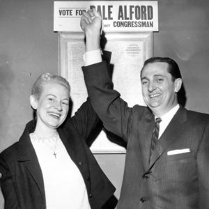 White man in suit and tie holding white woman's hand up with sign in background reading "Vote for Dale Alford for Congressman."