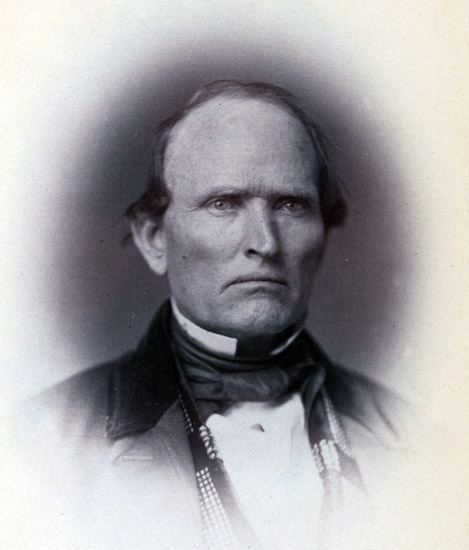 White man with stern expression in suit with white collar
