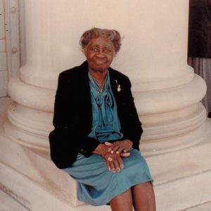 Older African-American woman in dress sitting at the base of a column