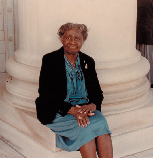 Older African-American woman in dress sitting at the base of a column