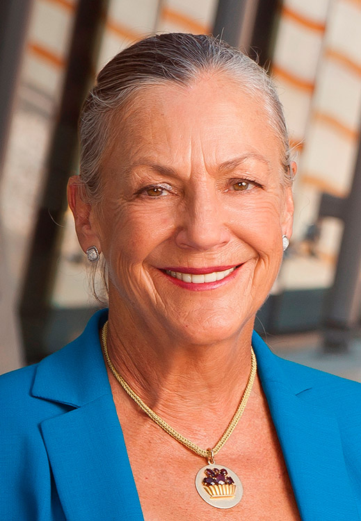 Older white woman smiling in blue suit with earrings and pendant necklace