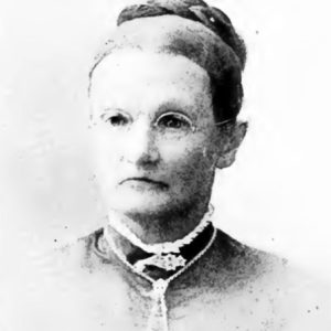 faded black and white photo of older white woman with round glasses in dress and necklace and a braided bun