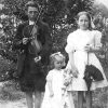White boy with fiddle standing next to white girl with umbrella and younger white girl with doll