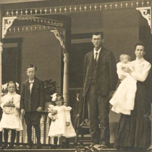 White man woman and three children on porch of their house