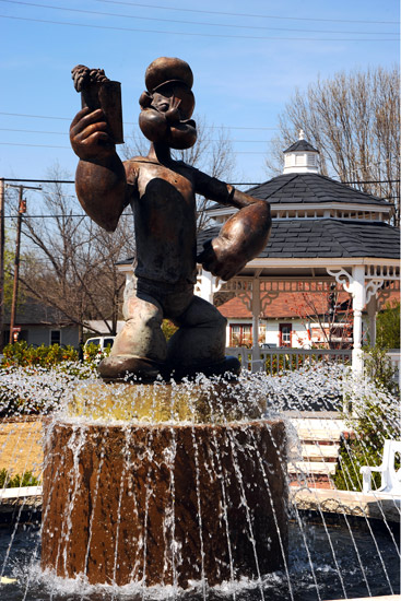 fountain with bronze statue of cartoon figure holding a can of spinach in front of gazebo